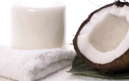 A close-up of a fresh coconut half next to a jar of coconut cream, resting on a white towel and green leaves, creating a refreshing food-themed HD desktop wallpaper.