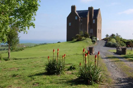 HD desktop wallpaper showcasing the man-made Dunduff Castle atop a grassy hill under a clear blue sky with surrounding greenery and a gravel path.
