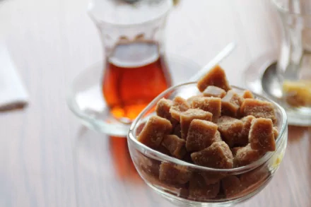 Close-up of brown sugar cubes in a glass bowl with a traditional tea glass filled with amber tea in the background, captured in vibrant 4K Ultra HD.