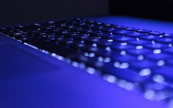 A close-up of a sleek keyboard illuminated by cool blue light, showcasing modern technology. This high-definition wall background adds a stylish touch to any desktop.