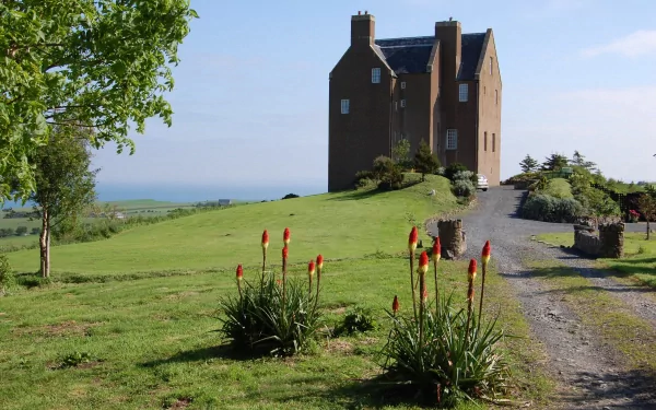 HD desktop wallpaper showcasing the man-made Dunduff Castle atop a grassy hill under a clear blue sky with surrounding greenery and a gravel path.