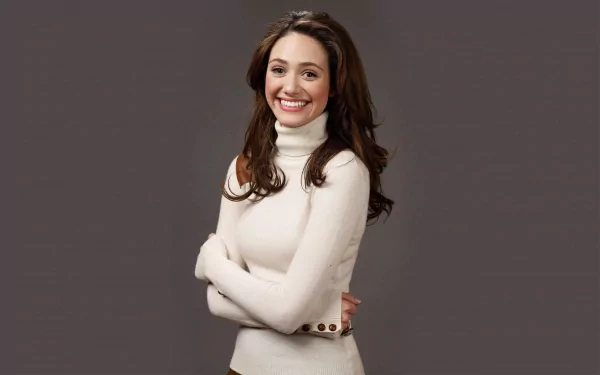 HD desktop wallpaper featuring celebrity Emmy Rossum smiling with arms crossed, wearing a white turtleneck against a plain gray background.