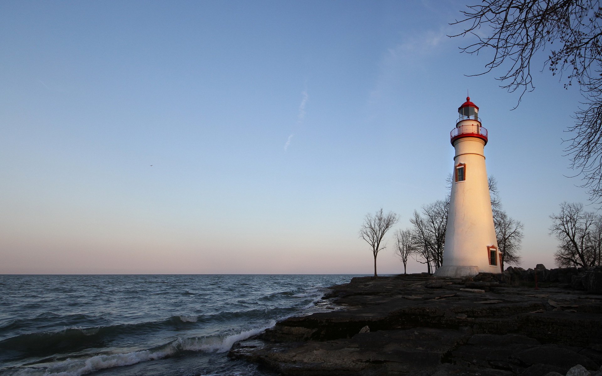 A serene HD wallpaper featuring a lighthouse standing by the shoreline, with gentle waves and a clear sky, capturing the beauty of man-made structures in nature.