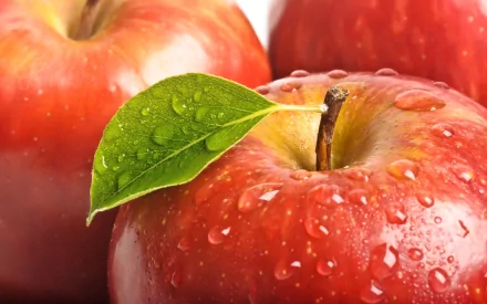 Close-up of dewy red apples with green leaves, showcasing their vibrant color and freshness, designed as a high-definition desktop wallpaper and background.