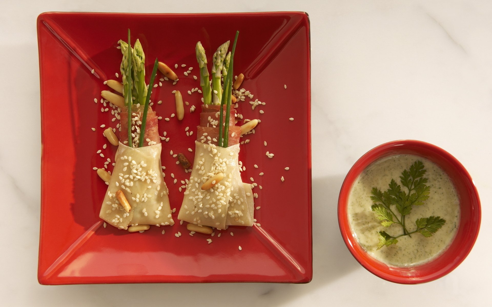 HD PC desktop wallpaper featuring a meal of asparagus wrapped in pastry on a red square plate, accompanied by a bowl of creamy soup garnished with fresh herbs.