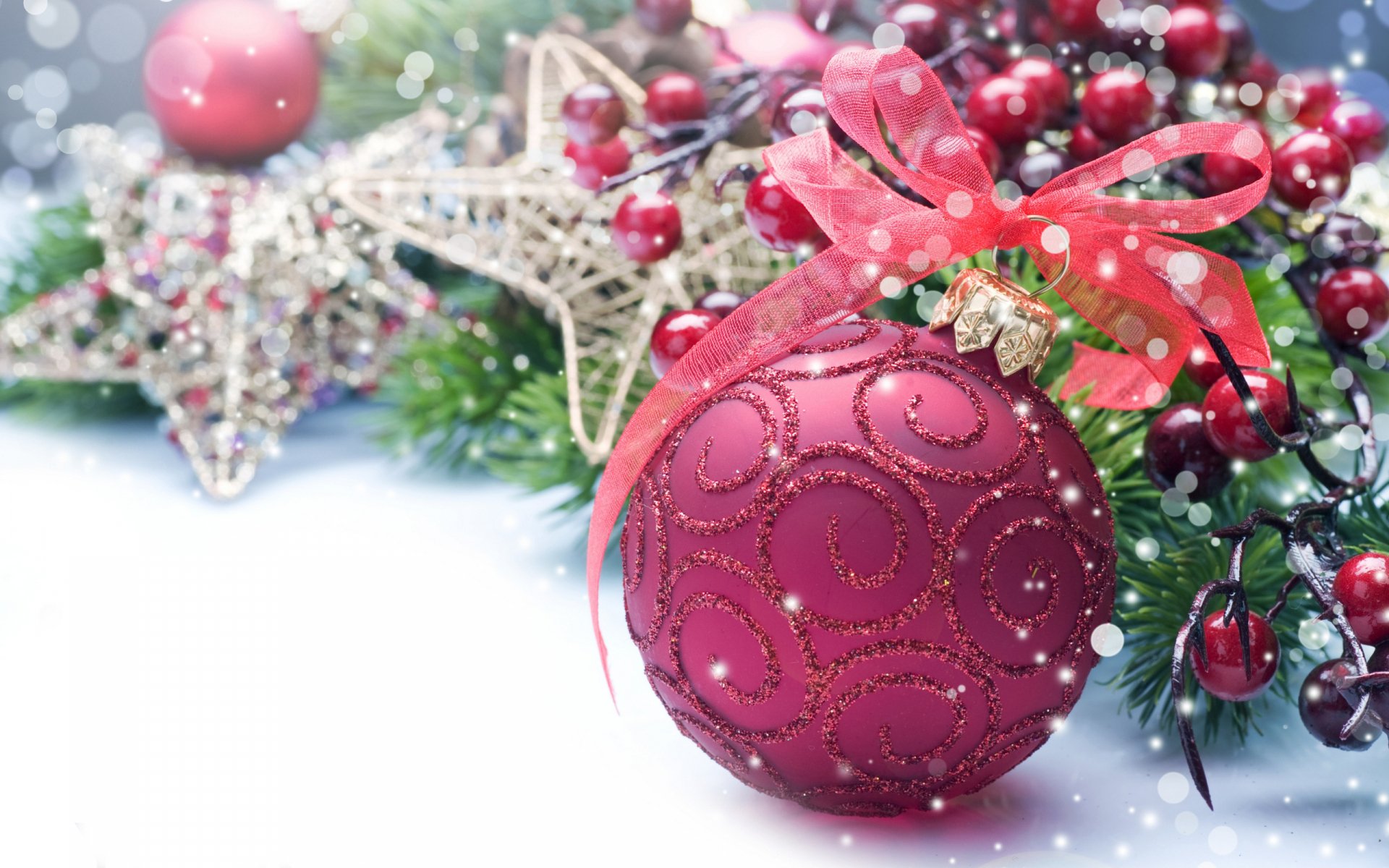A vibrant red Christmas ornament adorned with swirls and a bow rests among festive greenery and gold stars, evoking a warm holiday spirit. HD desktop wallpaper and background.
