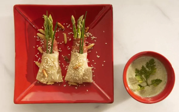 HD PC desktop wallpaper featuring a meal of asparagus wrapped in pastry on a red square plate, accompanied by a bowl of creamy soup garnished with fresh herbs.