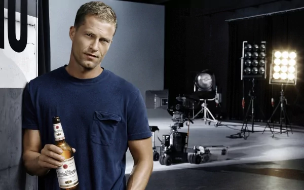 HD PC desktop wallpaper featuring celebrity Til Schweiger holding a beer bottle in a studio setting with professional lighting and camera equipment in the background.