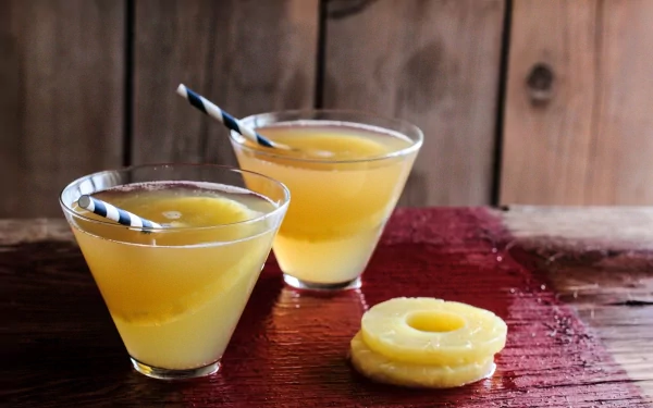 HD PC desktop wallpaper showing two yellow tropical drinks with striped straws and a pineapple slice on a wooden table, evoking a fresh, summery vibe.