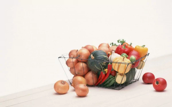 HD desktop wallpaper featuring a wire basket filled with onions, tomatoes, peppers, and squash against a clean white background.
