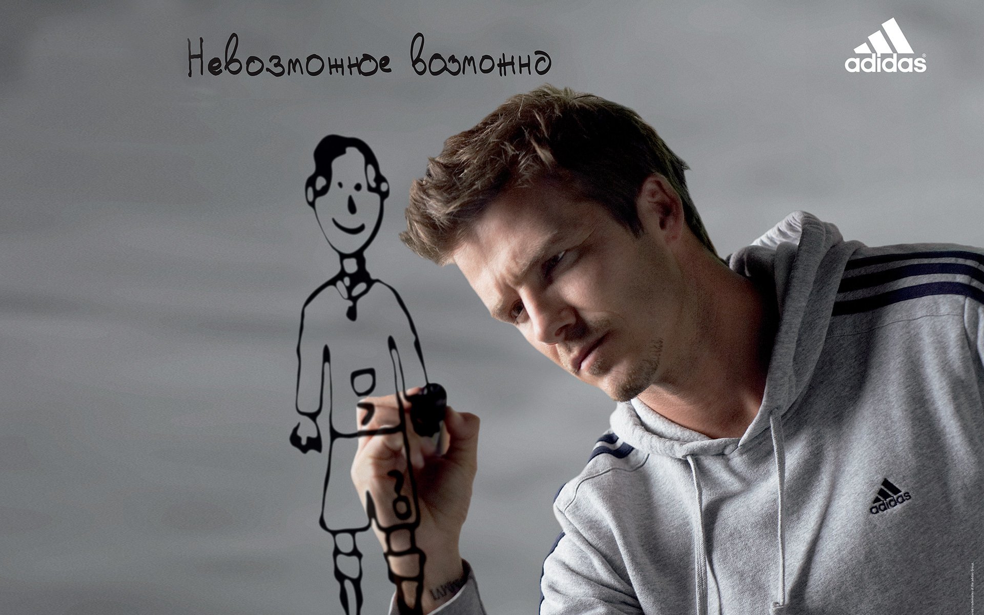 HD desktop wallpaper featuring sports icon David Beckham in an Adidas hoodie drawing a cartoon soccer player on a transparent board against a gray background.