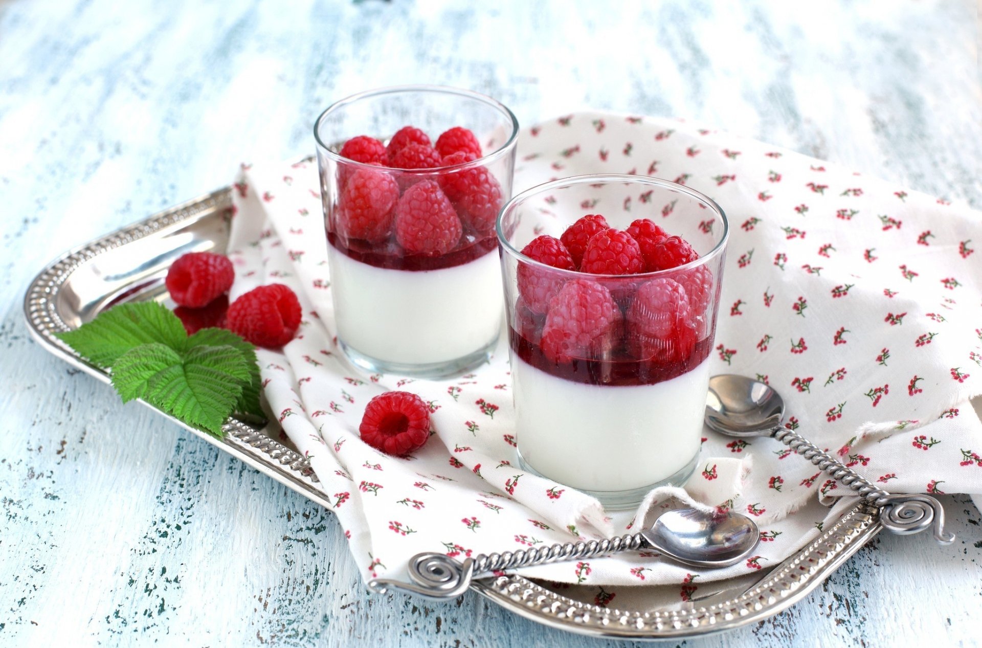Two elegant dessert glasses filled with creamy panna cotta and topped with fresh raspberries, arranged on a silver tray with a patterned napkin. A delicious food-themed HD desktop wallpaper.