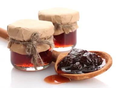 Close-up of dark fruit jam in a wooden spoon with two small glass jars wrapped in paper, captured in 4K Ultra HD as a vibrant food desktop wallpaper.