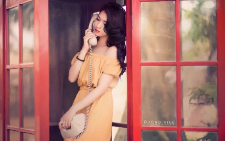 Asian woman in an off-shoulder dress, holding a vintage phone in a red phone booth. HD desktop wallpaper and background.