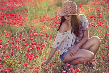 A woman in a straw hat and casual attire sits in a vibrant field of red flowers, creating a serene and contemplative mood. This HD desktop wallpaper captures the essence of tranquility and natural beauty.