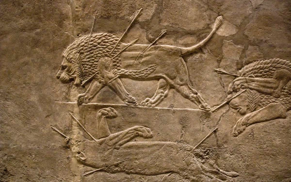 HD PC desktop wallpaper featuring an artistic Assyrian lion hunt relief carved in ancient stone, showcasing dynamic lions and hunters in motion.