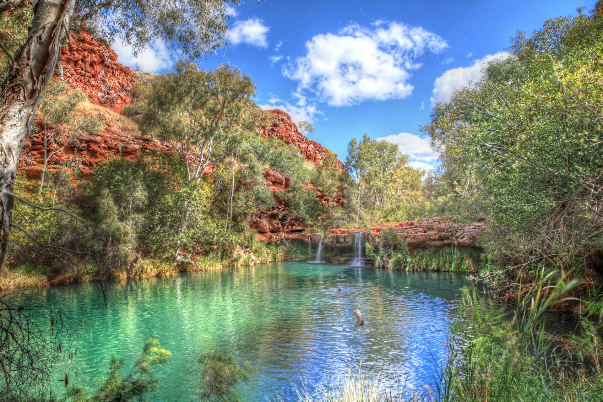 A serene fall scene featuring a clear pond beneath a waterfall, surrounded by vibrant trees and rocky formations, creating a tranquil nature setting. Perfect HD desktop wallpaper.