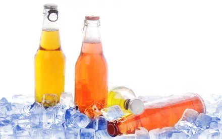 HD desktop wallpaper featuring three glass bottles of colorful drinks chilled on a bed of ice against a white background.