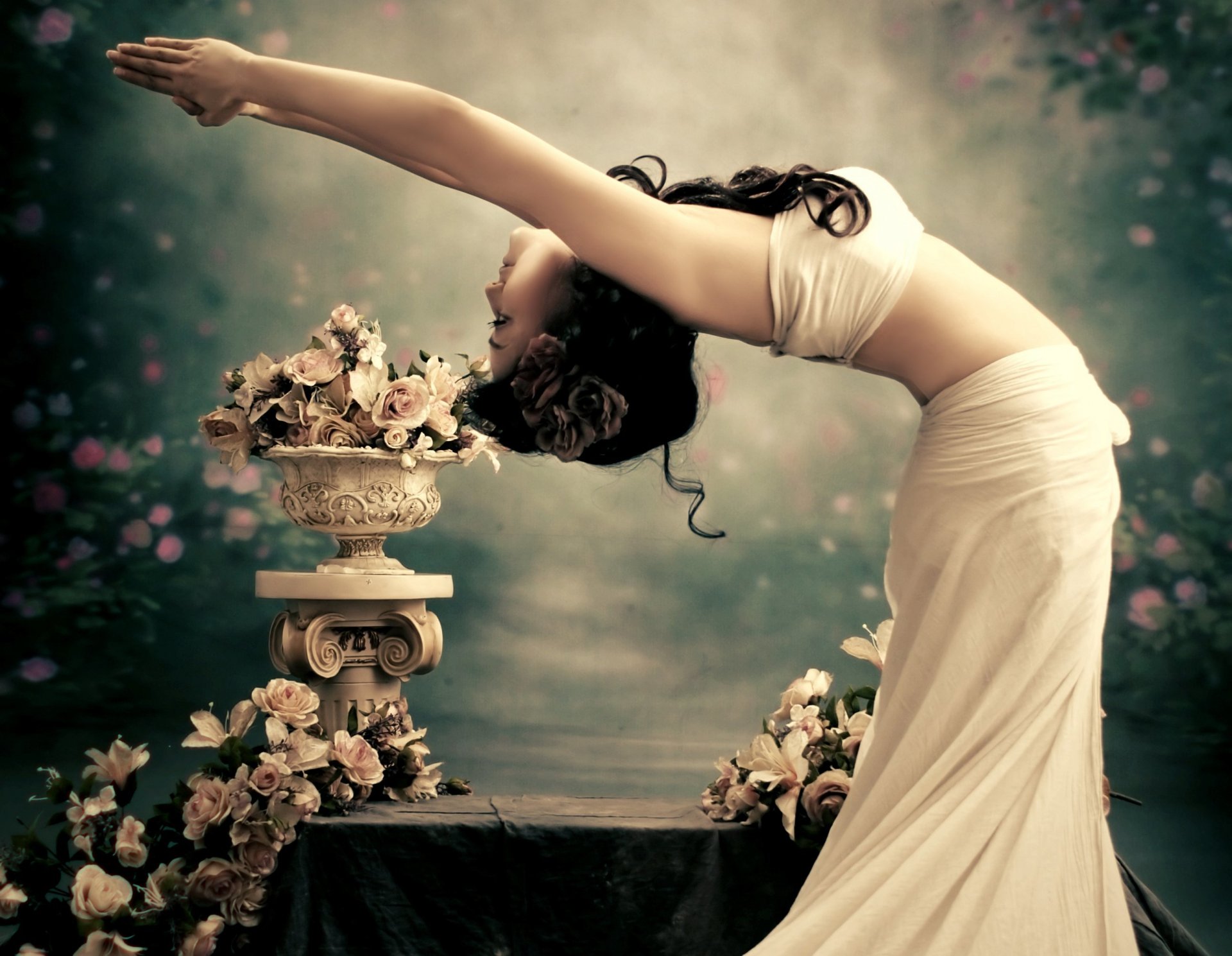 A graceful woman bends elegantly over a flower-adorned pedestal, capturing a serene mood in this HD desktop wallpaper. The soft colors enhance the tranquil atmosphere.