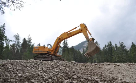 Yellow Liebherr 944 excavator vehicle on a rocky slope with bucket raised, forested mountains and cloudy sky backdrop — 4K Ultra HD PC desktop wallpaper/background.