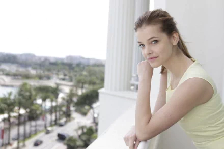 A stunning HD desktop wallpaper featuring celebrity Barbara Palvin, gazing thoughtfully while leaning on a balcony, with vibrant city scenery and palm trees in the background.