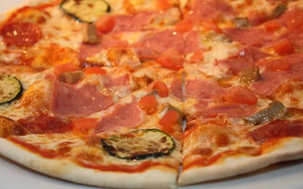 Delicious pizza topped with ham, tomatoes, and zucchini, set against a vibrant backdrop, captured in high definition for a captivating desktop wallpaper.