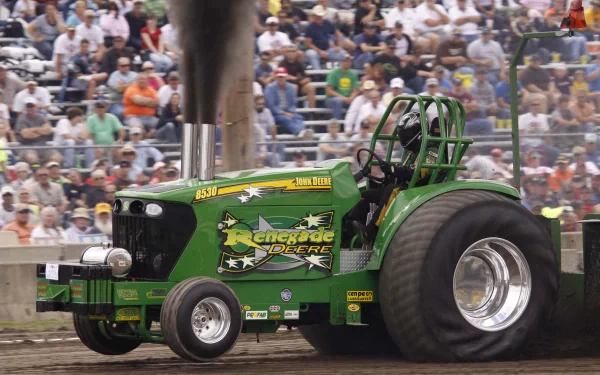 John Deere 8530 green tractor vehicle with oversized rear tires and smoke at a packed motorsport event — 2K Quad HD PC desktop wallpaper/background.