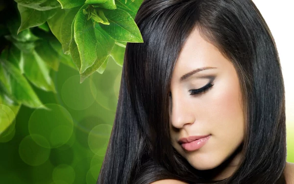 A serene woman with long, dark hair gazes downwards, framed by vibrant green leaves, creating a calming HD desktop wallpaper background.