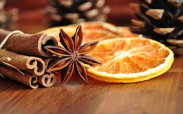 A close-up of cinnamon sticks, star anise, and dried orange slices on a wooden surface, complemented by pine cones in the background. A rich, warm-toned 4K Ultra HD wallpaper.