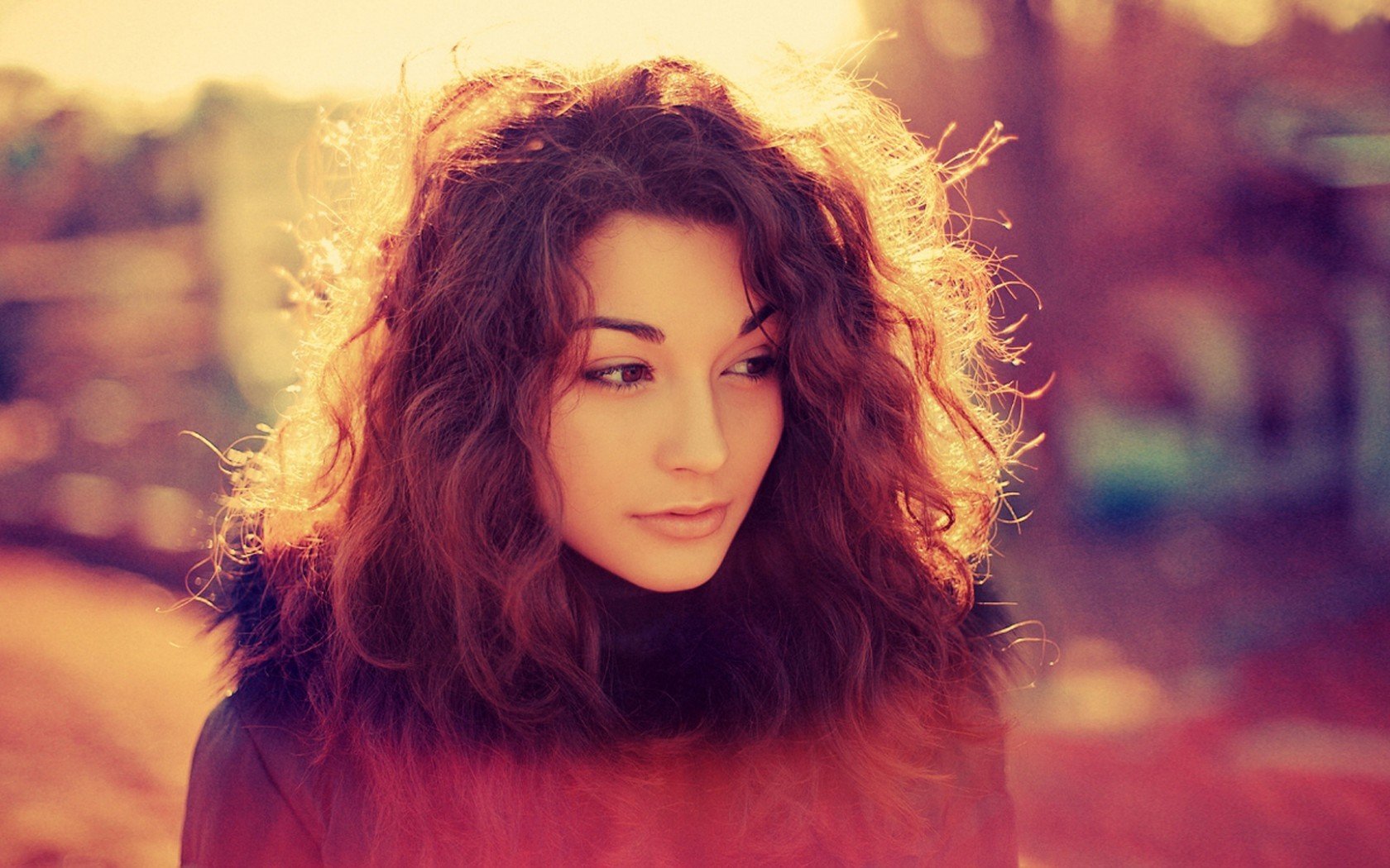 HD desktop wallpaper of a beautiful woman with curly hair, softly lit in warm tones creating a serene and captivating atmosphere.