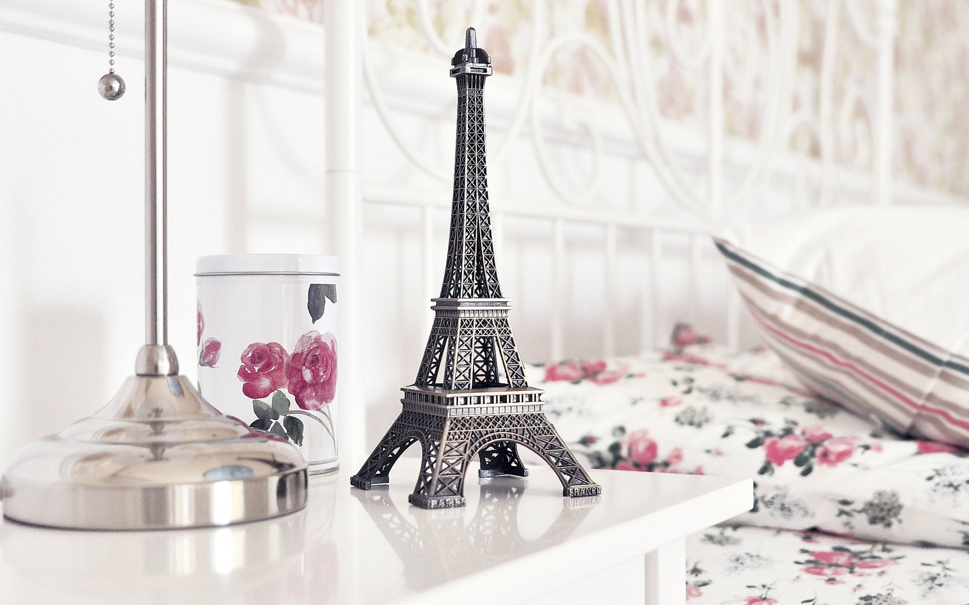 A still life photograph featuring a decorative Eiffel Tower figurine, a floral mug, and a bedside lamp, creating an elegant and charming atmosphere for a HD desktop wallpaper.