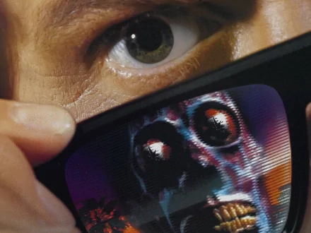 Close-up still from the movie They Live showing an eye above sunglasses reflecting a skeletal alien face — HD PC desktop wallpaper and background.