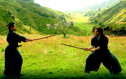 Two samurai in traditional attire engage in a duel in a lush green landscape, depicting a scene from the movie The Last Samurai. This serves as a stunning HD desktop wallpaper.