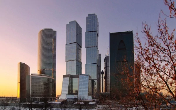 HD PC desktop wallpaper/background of man-made Moscow skyline at sunset, reflective modern skyscrapers rising behind snow and bare winter trees.