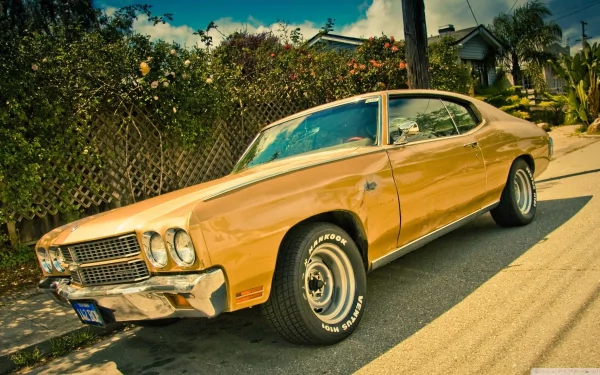 A striking yellow Chevrolet Chevelle SS parked on a sunny street, showcasing its classic muscle car design and gleaming features against a vibrant background.