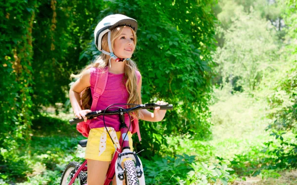 A child in a helmet smiles while holding a bicycle, surrounded by lush greenery, captured in vibrant photography, making for a delightful HD desktop wallpaper and background.