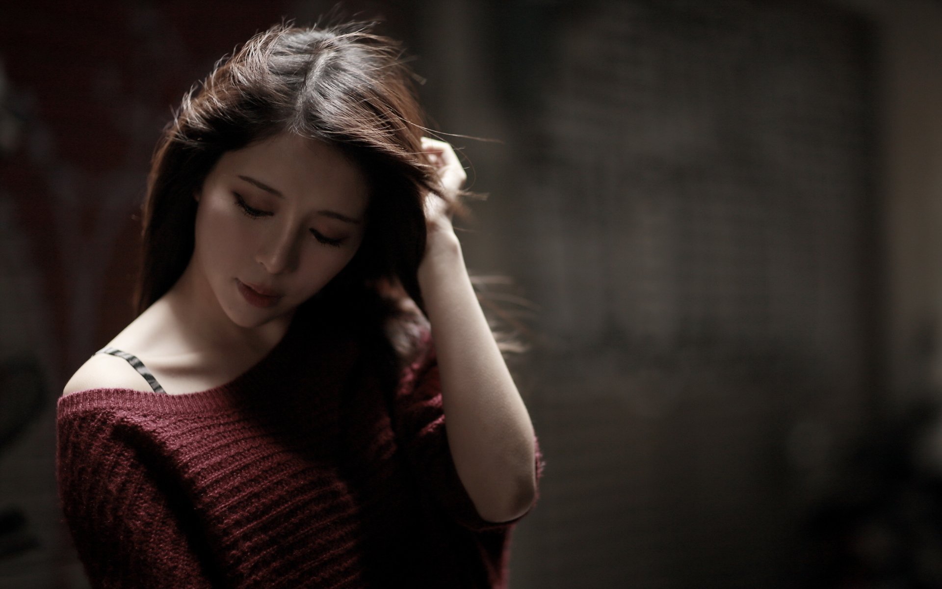 A woman in a deep red sweater poses thoughtfully, her long hair cascading as she gently touches it. This HD image serves as a striking desktop wallpaper and background.