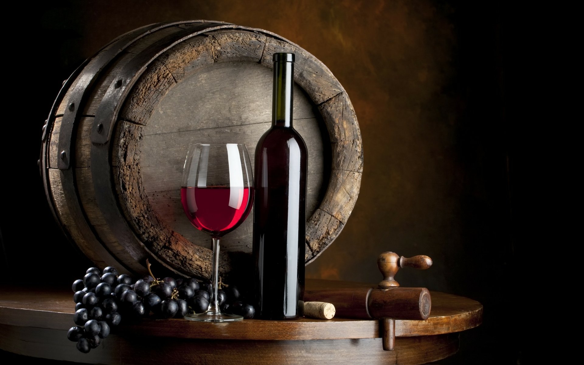 HD PC desktop wallpaper featuring a wine bottle, glass of red wine, grapes, corkscrew, and a rustic wooden barrel in a warm, dark setting.
