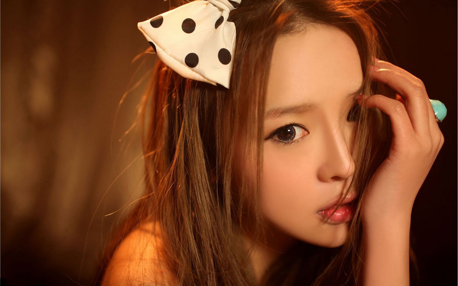 HD desktop wallpaper featuring a woman with long hair, wearing a polka dot ribbon accessory. She has a thoughtful expression and is looking directly at the camera.