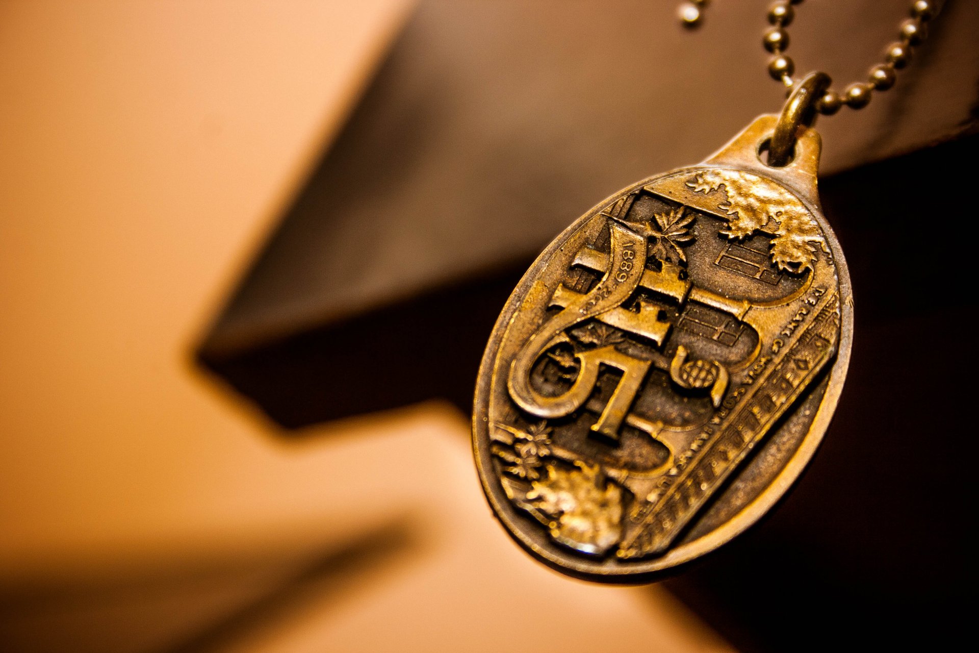 Close-up of a detailed vintage pendant on a chain, captured in a warm tone. This 4K Ultra HD PC desktop wallpaper highlights intricate textures and craftsmanship.