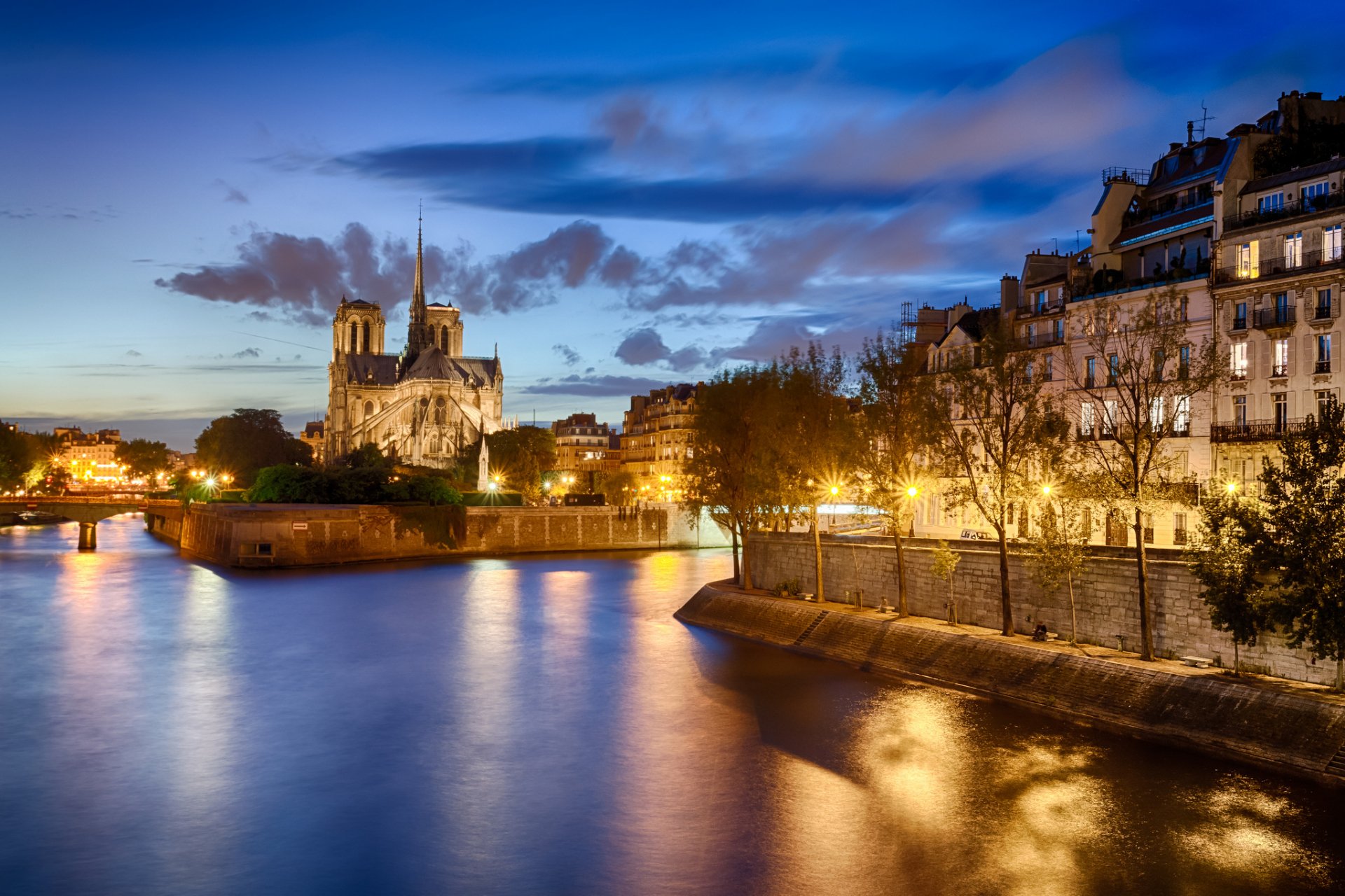 A stunning HD wallpaper featuring Notre-Dame de Paris at dusk, illuminated along the Seine, highlighting the beauty of this iconic religious landmark in Paris.
