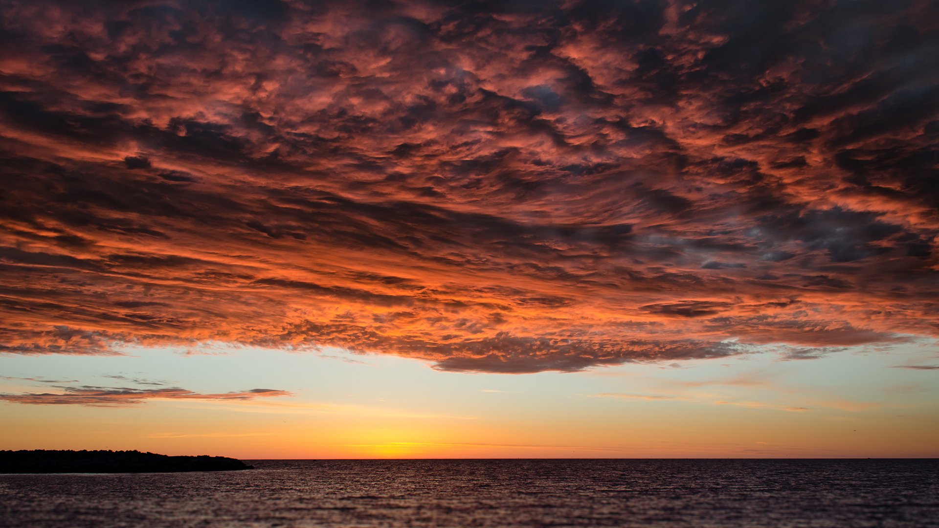 HD desktop wallpaper showcasing a dramatic sunset with vibrant orange clouds over a calm sea, blending nature and cloud elements.