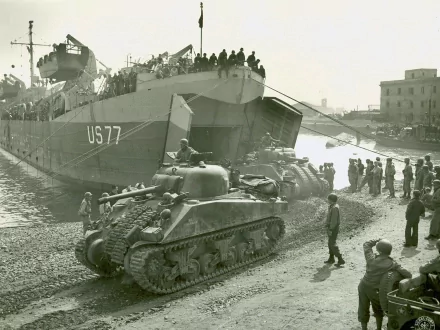Military scene: M4 Sherman tank rolling off landing ship US77 onto a crowded dock, soldiers and civilians watching — 2K Quad HD PC Desktop Wallpaper and Background.