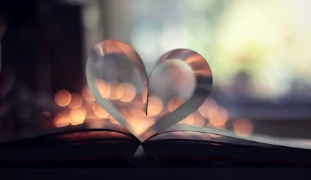 A beautifully lit image of an open book with pages shaped into a heart, surrounded by soft bokeh lights, creating a warm and inviting atmosphere for a desktop wallpaper.