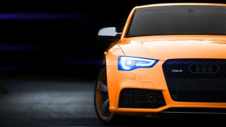 HD PC desktop wallpaper featuring the front view of a vibrant orange Audi vehicle with illuminated headlights against a dark background.