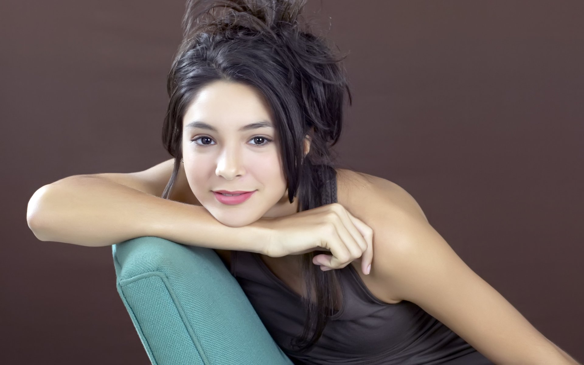 Portrait of a woman with a relaxed pose, leaning on a cushion against a brown background. This HD image serves as a desktop wallpaper and background.