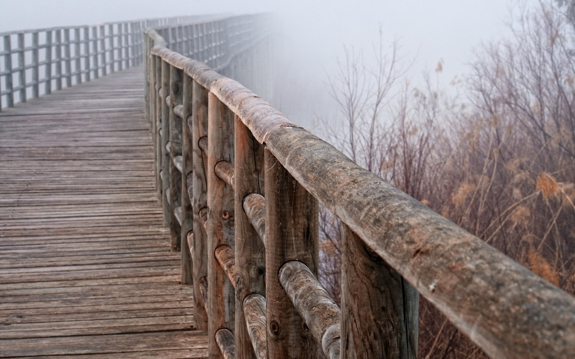 A serene wooden bridge extends into a foggy landscape, showcasing man-made craftsmanship amidst nature. This HD desktop wallpaper adds a tranquil touch to any background.