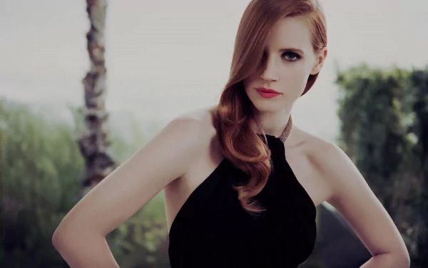 Jessica Chastain poses elegantly in a stylish black dress, showcasing her signature red hair against a serene outdoor backdrop. This HD image serves as a captivating desktop wallpaper.