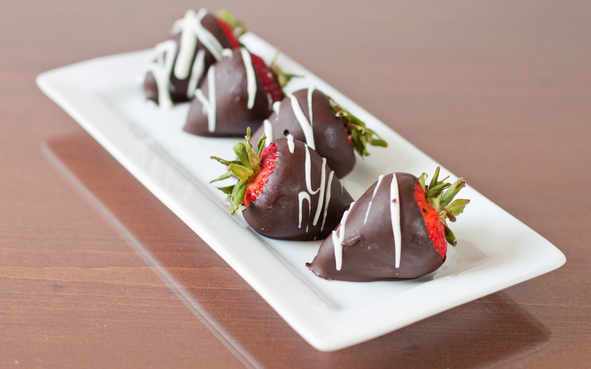 HD desktop wallpaper featuring a close-up of fresh strawberries dipped in chocolate with white drizzle, arranged neatly on a white rectangular plate.