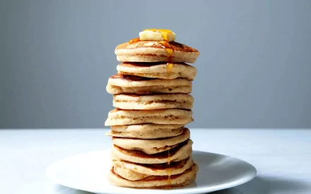HD desktop wallpaper featuring a tall stack of fluffy pancakes topped with a pat of butter and drizzled with syrup on a white plate against a gray background.